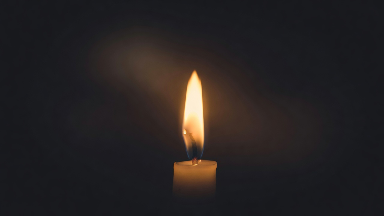 Close-up of a single candle flame glowing against a soft dark background with shallow depth of field